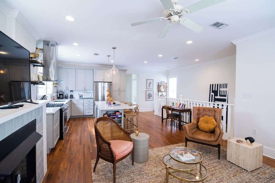 Gather and relax in this open-concept main floor layout featuring a living area with a fireplace, television, accent armchairs, and coffee table, seamlessly adjoining a kitchen equipped with a island counter and stainless steel appliances.