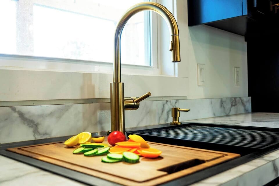 Double bowl sink with drop-in cutting board and drying rack and gold accents.