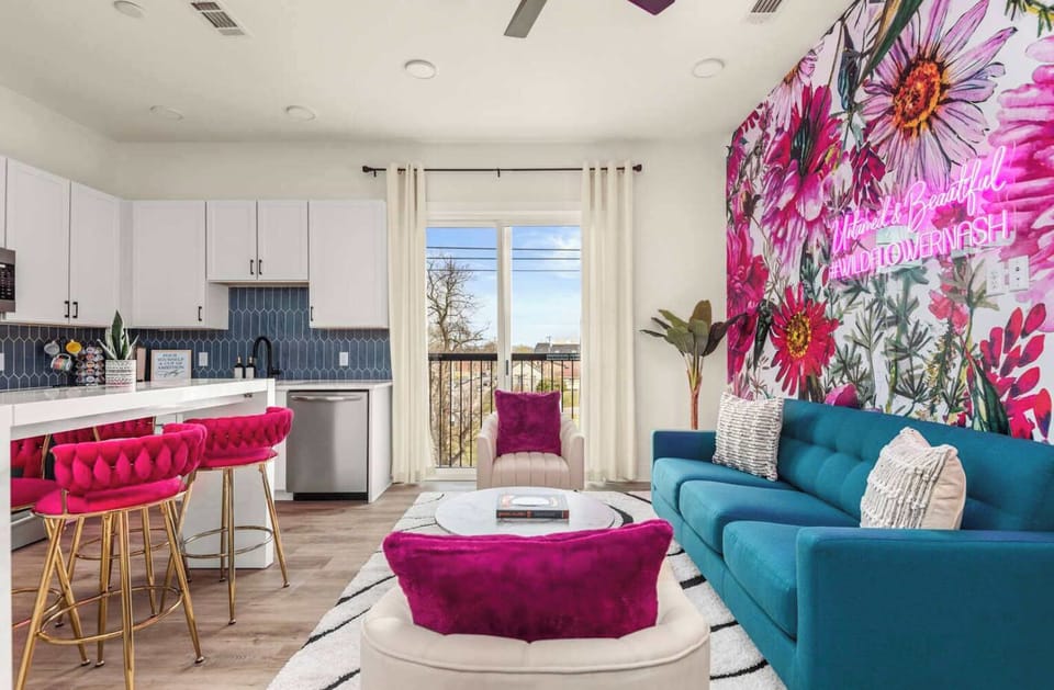 Living Room: A bright and inviting lounge area with a striking floral feature wall, cozy seating, and a neon sign for extra personality.