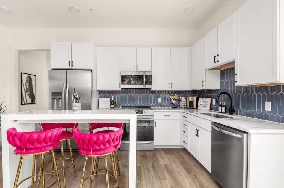 Kitchen: Cook in a modern kitchen with stainless steel appliances, a sleek backsplash, and bold pink barstools.