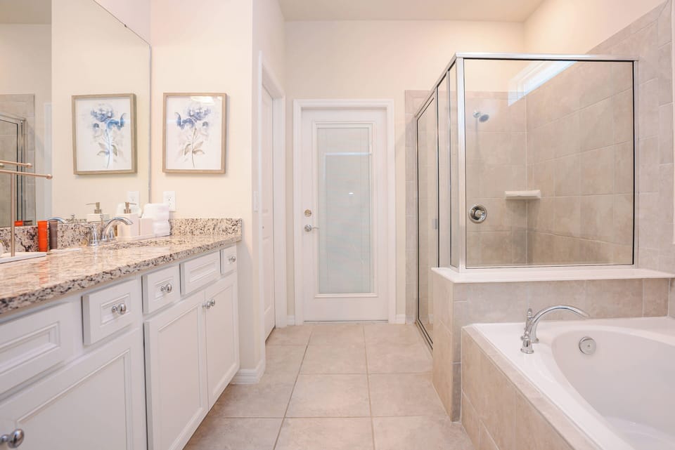 Step into a bright bathroom featuring elegant granite countertops and a spacious soaking tub. The glass-enclosed shower adds a modern touch, while soft colors and floral artwork create a refreshing atmosphere for your stay.