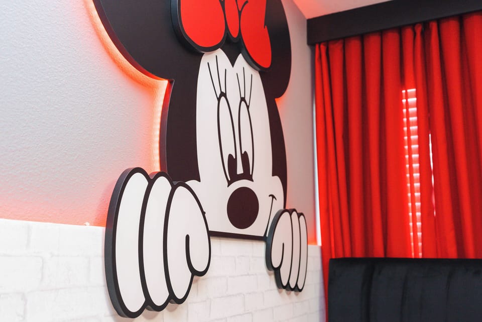 Bright red curtains frame a playful wall art piece featuring a cheerful character, creating a lively atmosphere. The unique decor adds a touch of whimsy, making this space an exciting choice for guests of all ages.