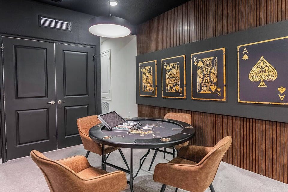 Step into a stylish game room featuring a sleek, round table surrounded by warm, brown chairs, perfect for friendly competition. The dark wood paneling and striking card-themed artwork create a unique atmosphere for fun evenings.