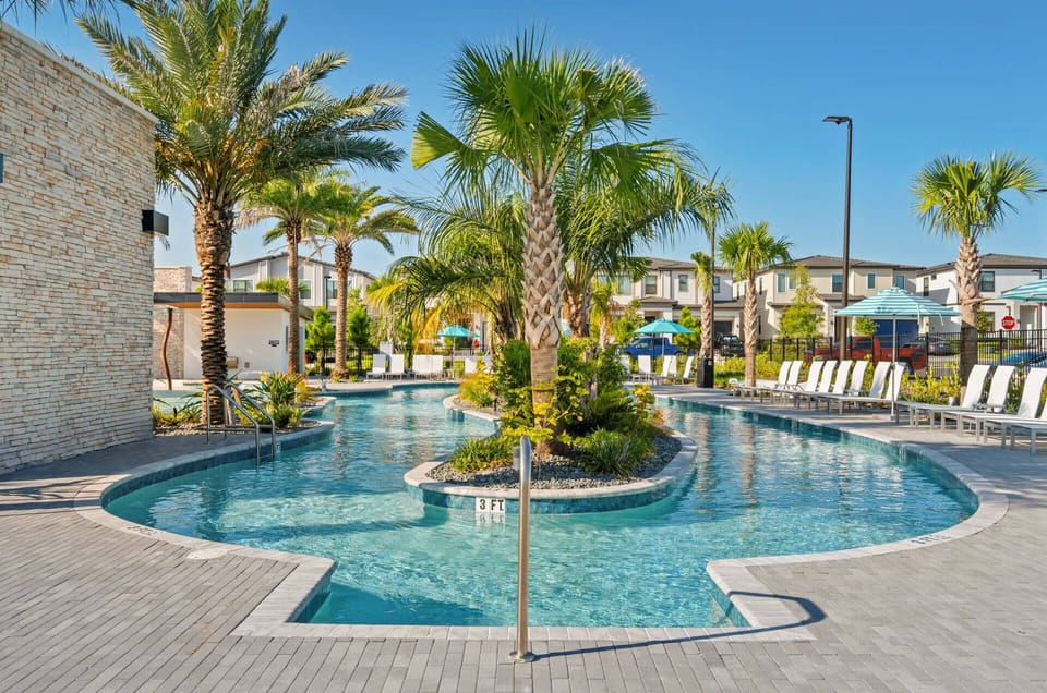 Relax by the stunning pool surrounded by swaying palm trees and vibrant landscaping. The inviting water glistens under bright blue skies, while comfortable lounge chairs offer the perfect spot to soak up the sun.