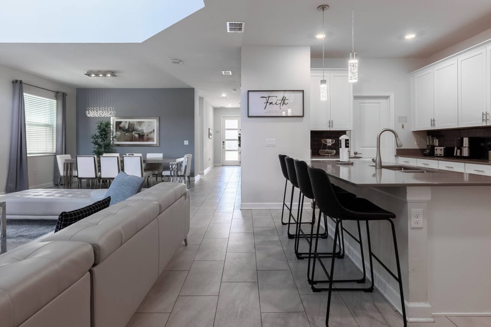 Experience a stylish open-concept living space where sleek black bar stools complement a chic kitchen with modern cabinetry. Natural light brightens the elegant dining area, inviting you to relax in comfort.