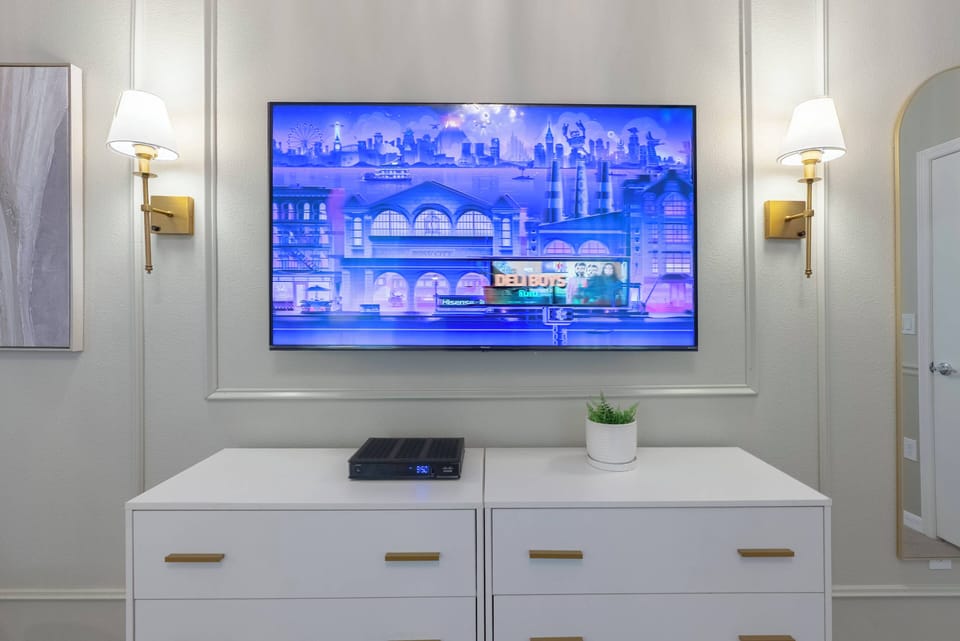 Enjoy a cozy evening in the living room, where a stylish white media console pairs beautifully with soft gray walls. The warm sconces create a welcoming ambiance, and the large TV invites you to unwind with your favorite shows.
