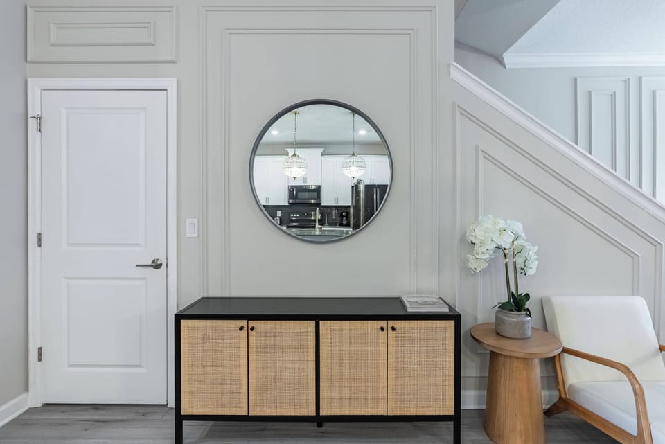 Welcome to a stylish entryway adorned with a chic circular mirror that captures the home's modern vibe. A textured rattan storage cabinet brings warmth, while a sleek wooden accent table beckons you to relax after your adventures.