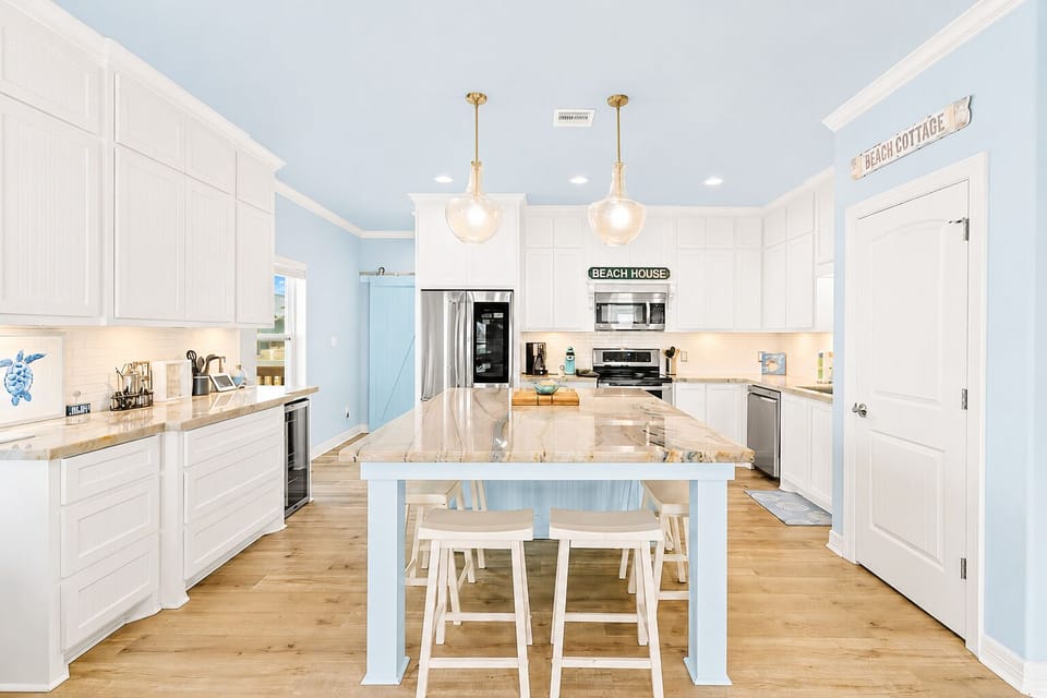 Bright vacation rental kitchen with white cabinetry, stainless steel appliances, pendant lighting and a large center island with counter seating.