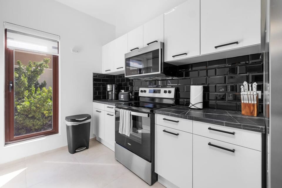 Cook in style in this sleek kitchen, featuring modern white cabinetry, black backsplash, and high-end appliances. A window brings in natural light, enhancing the clean and vibrant space.
