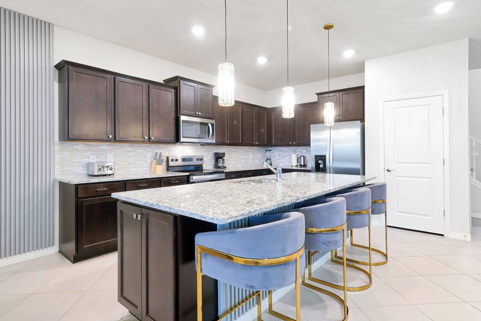 Experience a beautifully designed kitchen with dark cabinetry and a spacious granite island. Modern bar stools add sophistication, while bright overhead lighting creates a warm and inviting atmosphere for your culinary adventures.