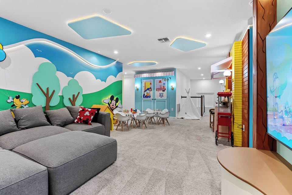 Bright colors and playful decor fill this spacious living area, where a cozy gray sectional invites you to relax. The cheerful mural adds a whimsical touch, making it ideal for family gatherings and enjoyable evenings together.