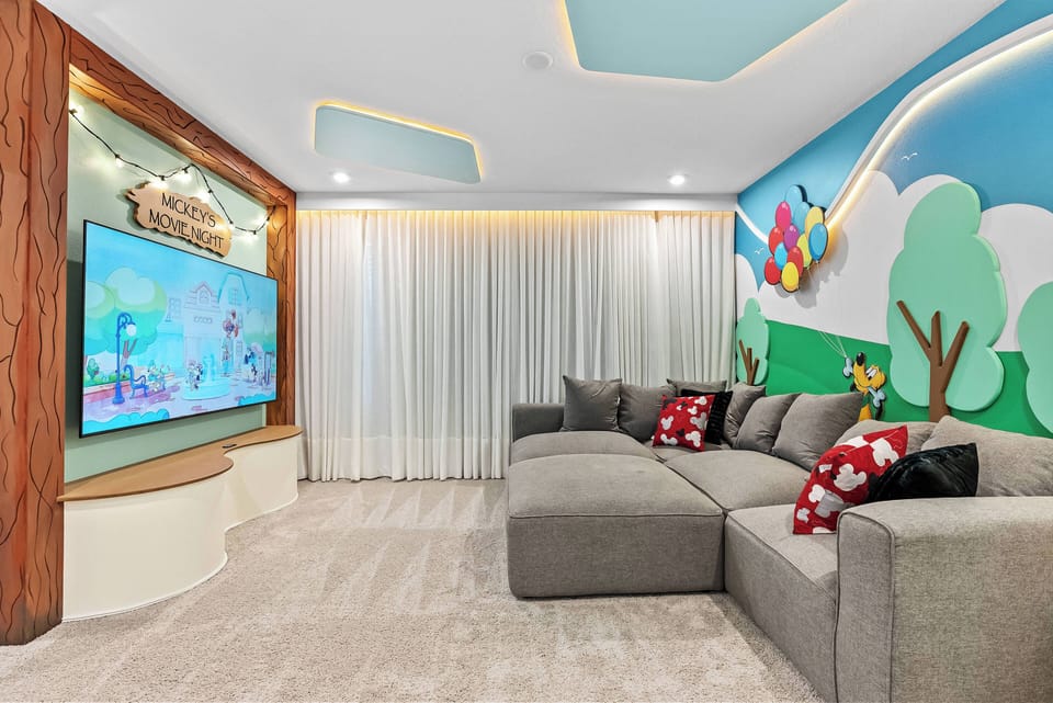 Experience this lively family room with cozy gray seating in a welcoming corner, ideal for movie nights. A playful mural and soft lighting set the perfect atmosphere for relaxation and fun for guests of all ages.