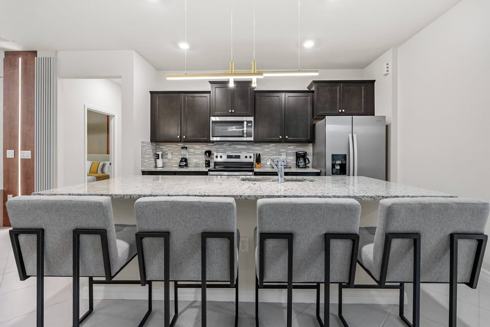 Enjoy a stylish kitchen with dark cabinetry and a spacious granite countertop, perfect for gatherings. Modern bar stools add a chic touch, making it ideal for casual meals or enjoying your morning coffee in this inviting space.