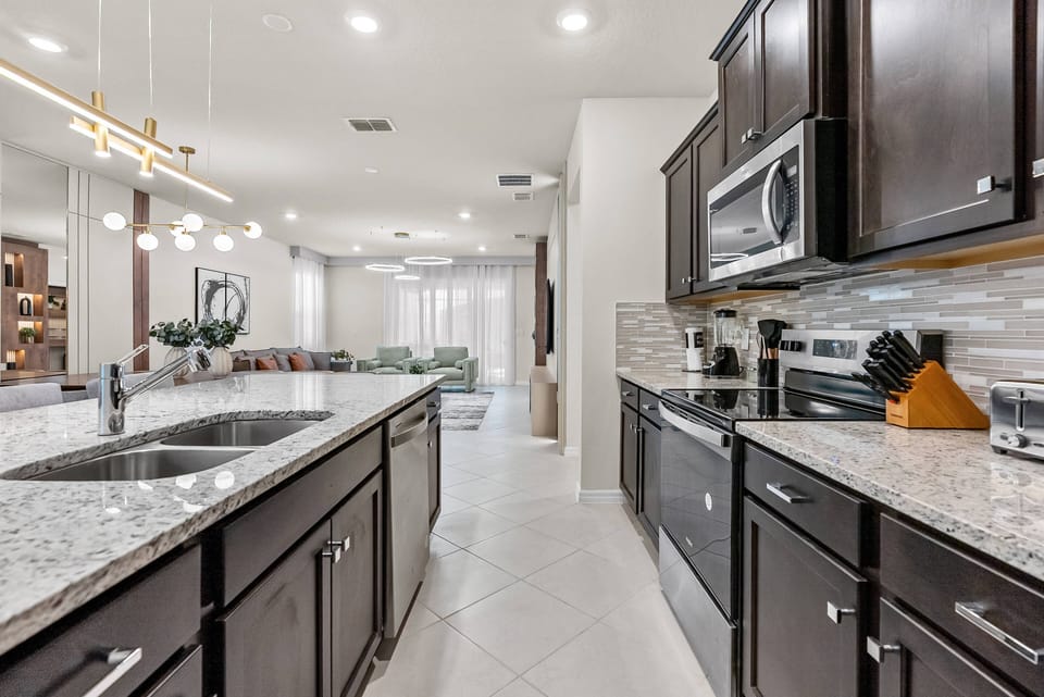 Welcome to a beautifully designed kitchen with rich dark cabinetry and stunning granite countertops. Natural light enhances the sleek appliances and modern fixtures, making it a warm and inviting space perfect for cooking and.
