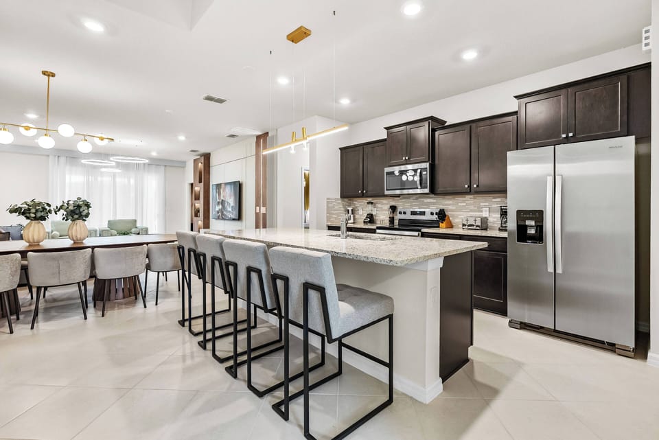 Experience a stunning kitchen with dark wood cabinets and light marble countertops, complete with a spacious island for stylish seating and modern stainless-steel appliances, ideal for cooking and entertaining guests.