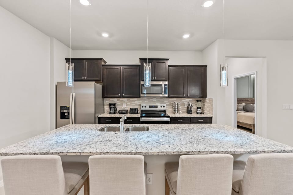 Enjoy a modern kitchen featuring rich dark wood cabinetry and gorgeous granite countertops. The spacious island with stylish bar stools is perfect for casual dining, and pendant lights add a warm, inviting touch to the atmosphere.
