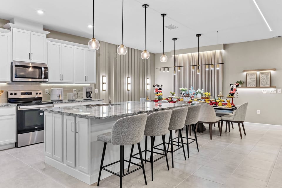 Welcome to a stylish kitchen with sleek gray cabinetry and a spacious island perfect for gatherings. Warm pendant lighting creates a cozy atmosphere in the elegant dining area, enhanced by vibrant decor for delightful meals.