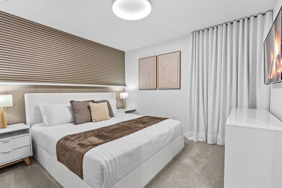 Relax in this cozy bedroom featuring a plush white bed layered with soft earth-toned linens. The textured wall behind the bed adds depth, complemented by sleek nightstands and contemporary art that enhances the tranquil ambiance.
