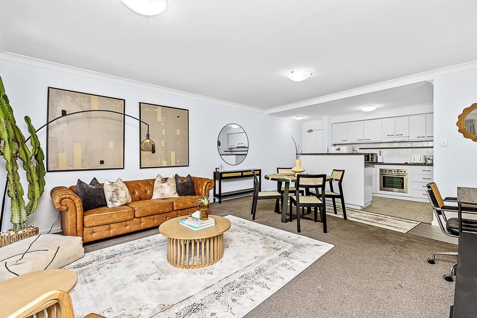 Experience modern living with a comfortable living room, showcasing a tufted leather sofa and a view of the well-equipped kitchen.