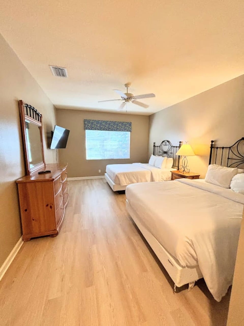 Comfortable bedroom with two beds, wood-look flooring, dresser storage, and a bright, relaxing layout.