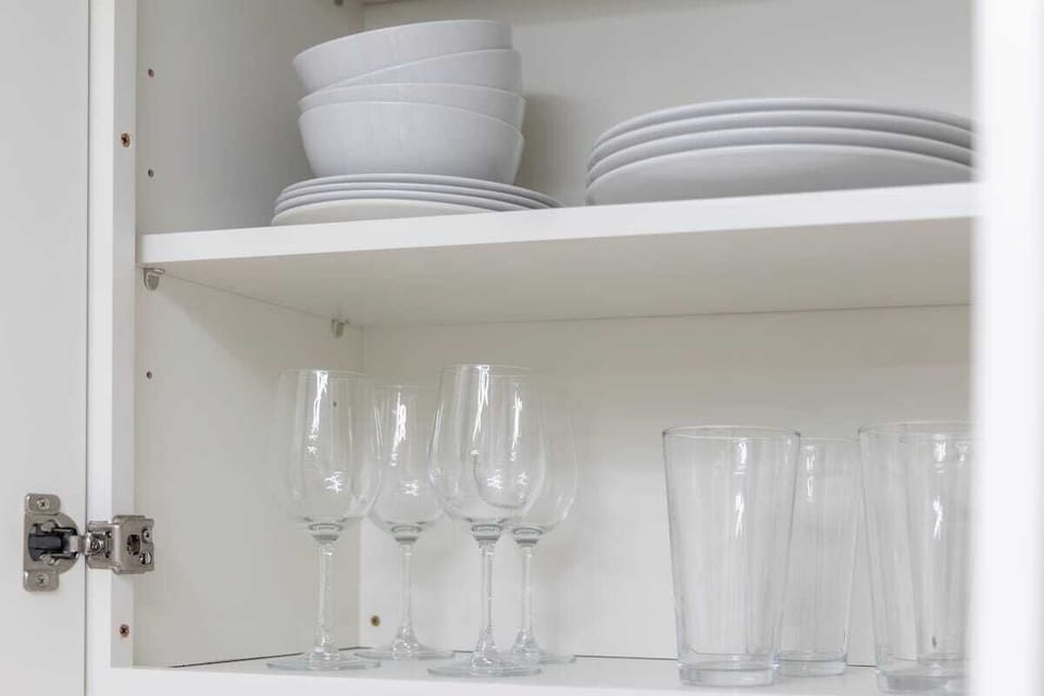 A cabinet stocked with clean white bowls, plates, and a variety of glassware.