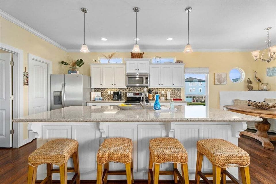 Spacious kitchen island with bar stools, pendant lighting, and open dining area designed for entertaining family and friends at the beach.