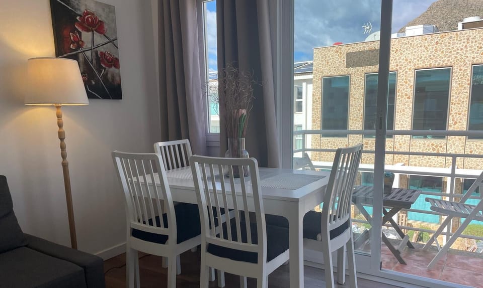 Bright dining area next to a large window with access to the balcony, featuring a white table and chairs, ideal for enjoying meals with natural light in this Puerto Pollensa holiday apartment.