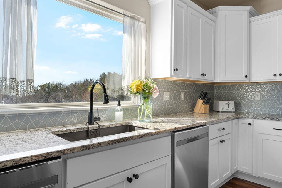 - Wash up or prep a meal with a peaceful view of trees and sky just beyond the window
- Let the sunlight pour in while you enjoy the little touches like flowers and soft curtains
- Every part of this kitchen brings calm, charm, and a homey feel