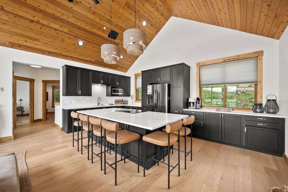 Your gourmet kitchen features sleek dark cabinets, a spacious island with seating for six, and stunning wood-beam ceilings that create a warm, inviting atmosphere.