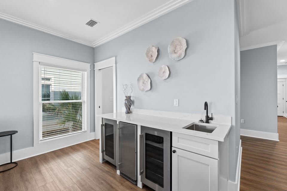 Enjoy your morning coffee in this elegant wet bar with sleek white counters, a modern black faucet, and stylish beverage fridges to keep drinks perfectly chilled.