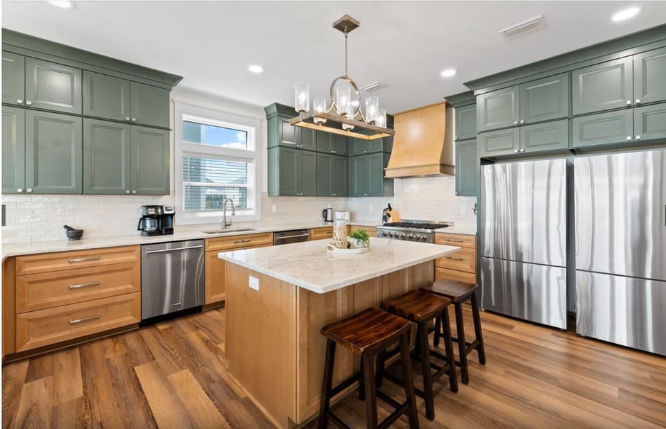 Your gourmet kitchen features stunning green cabinetry, warm wood accents, and premium stainless appliances—perfect for preparing memorable meals during your stay.