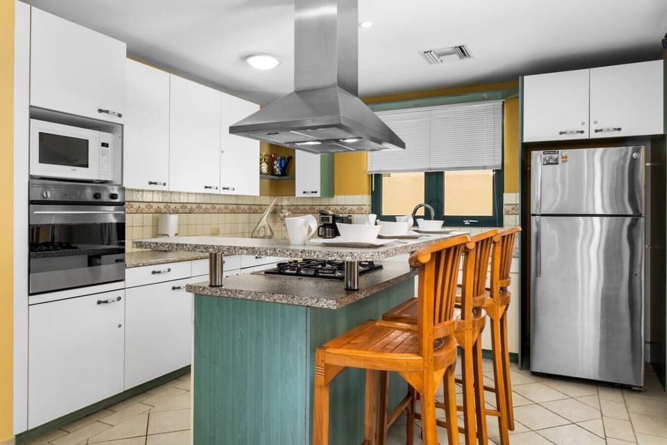 A cozy kitchen area with three barstool chairs, featuring a sleek refrigerator, oven, and stove, perfect for casual meals and drinks in a compact space. 🍽️🍷