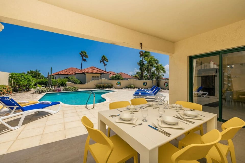 A beautiful dining area overlooking a sparkling pool, with sun loungers nearby, offering the perfect blend of relaxation and outdoor dining under the sun.
