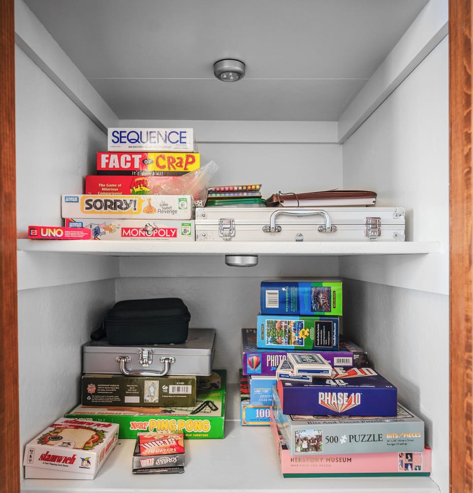 White cabinet with wood trim storing board games and puzzles.

