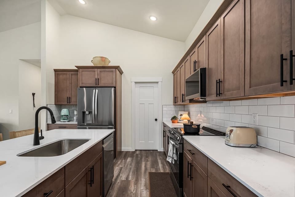 Another angle of this stunning kitchen showcases its thoughtful design and functionality. From the deep farmhouse sink to the stylish matte black fixtures, every detail has been curated for a comfortable stay. 