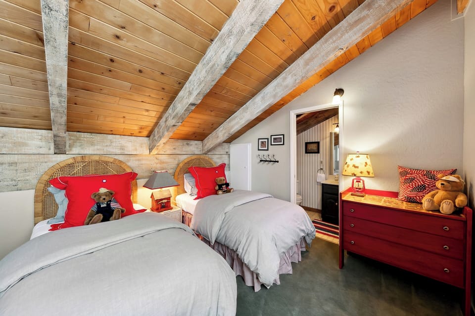 Your cozy twin room awaits with rustic beams, cheerful red accents, and teddy bear companions for a perfect alpine retreat.