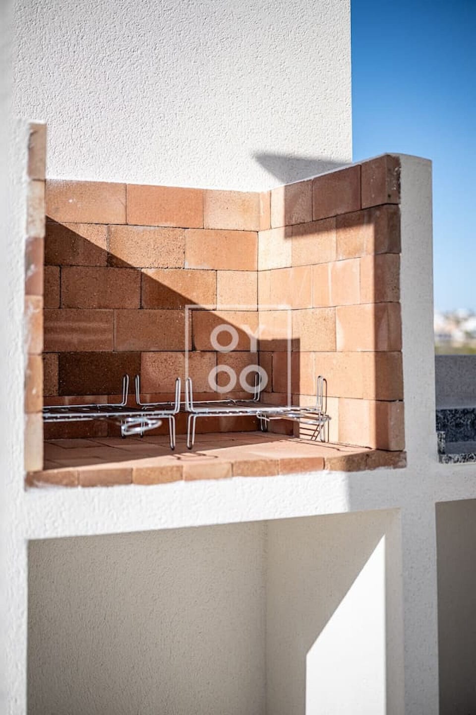 Built-in brick barbecue features a spacious grill area with sturdy metal grate and stucco finish. Ample open shelving underneath provides storage for firewood or tools, making it perfect for outdoor cooking and entertaining under clear skies. 🔥🍖🌞