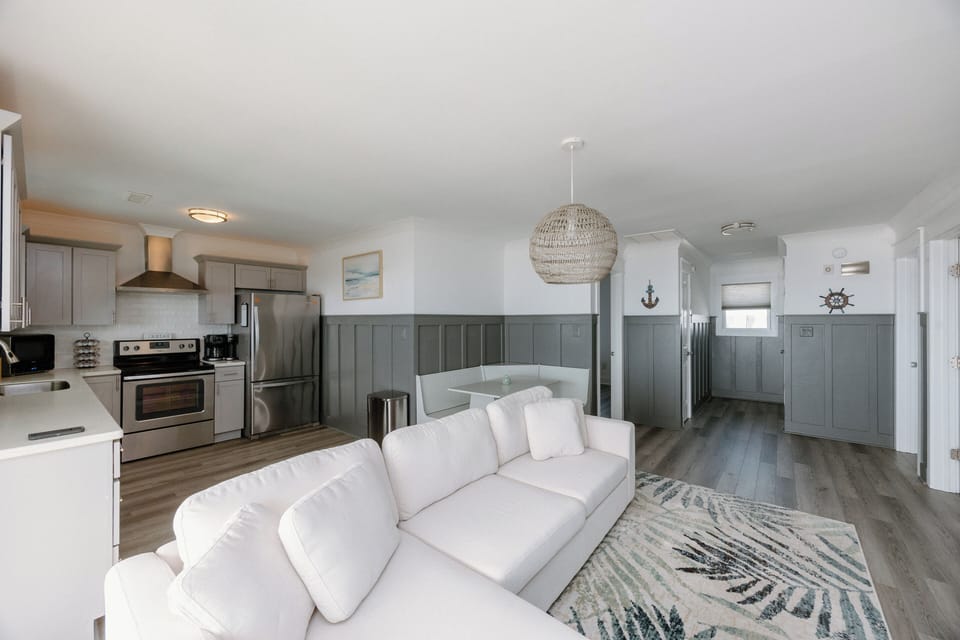 Bright and newly furnished living area featuring large ocean‑view windows, cozy seating, and a Smart TV.