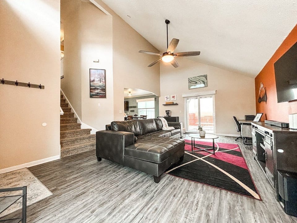 The main level features a bright and comfortable living room with a large sectional sofa, 4K Smart TV, sound system, and a dedicated workspace