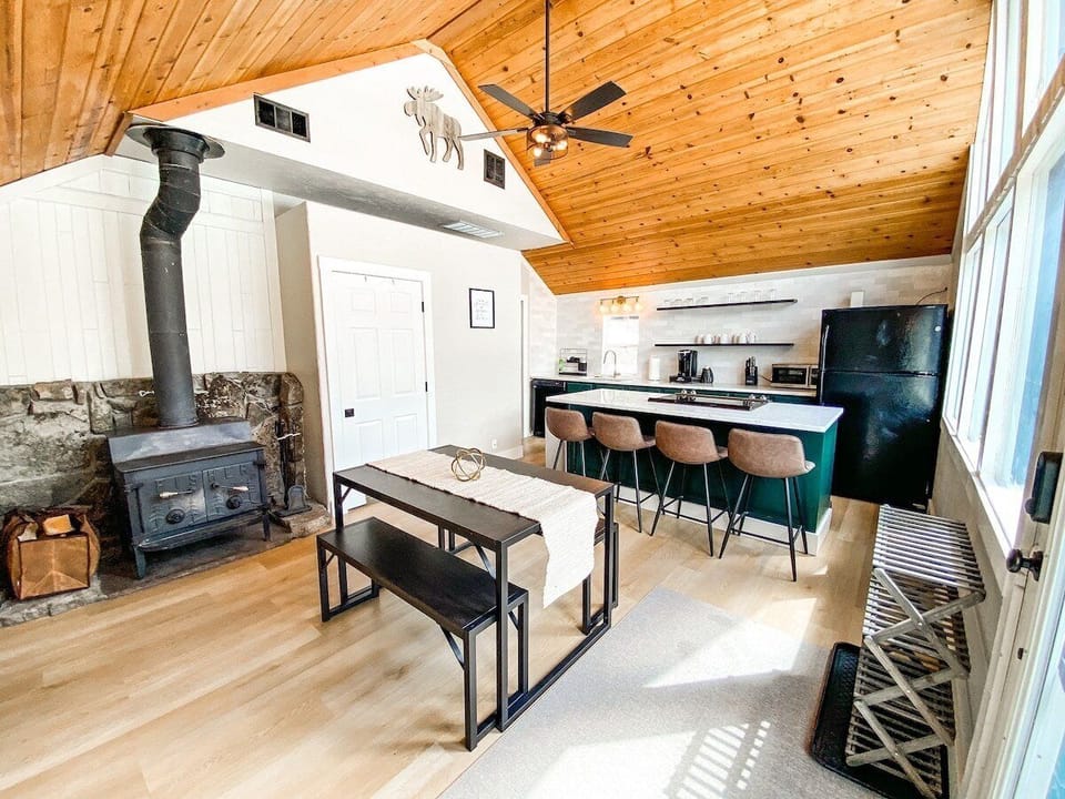 The fully equipped kitchen includes everything needed to prepare meals at home, featuring a large island with bar seating, a dedicated dining area, and a wall of windows overlooking the mountains.