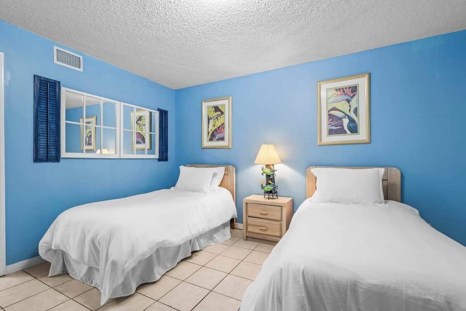 Enjoy a relaxing stay in this well-lit twin bedroom, complete with a dresser, a TV, and a mirror. The soft blue tones and beach-inspired décor create a peaceful and cozy atmosphere for a restful night’s sleep.