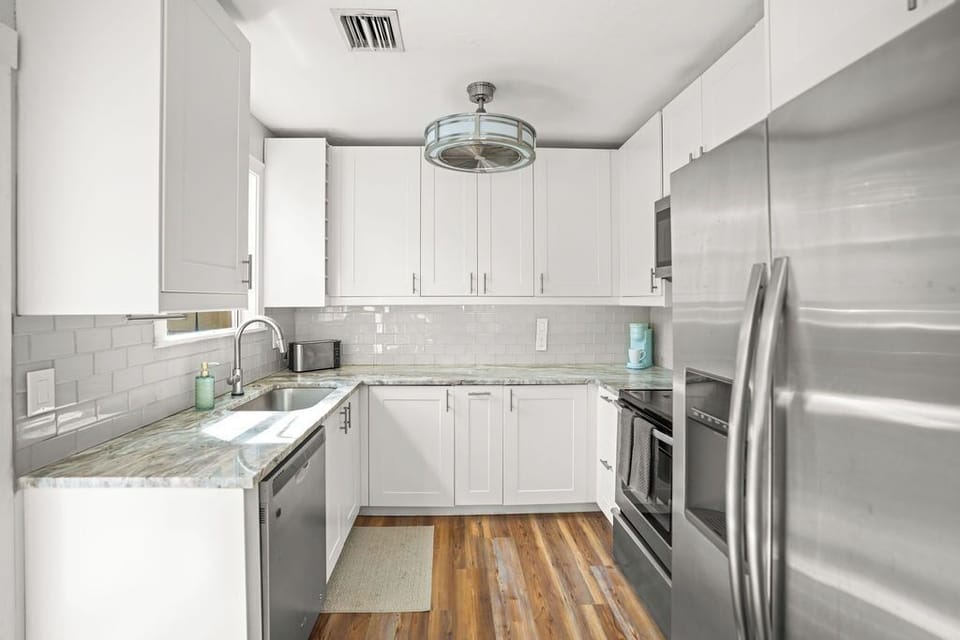 This modern fully-equipped kitchen features sleek white cabinetry, marble countertops, stainless steel appliances, and a stylish subway tile backsplash.
