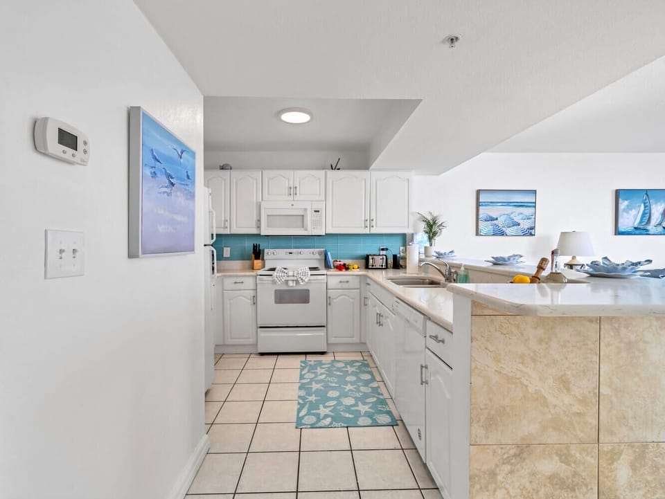 Your bright coastal kitchen awaits with white cabinets, turquoise accents, and charming nautical artwork to inspire beachside cooking adventures.