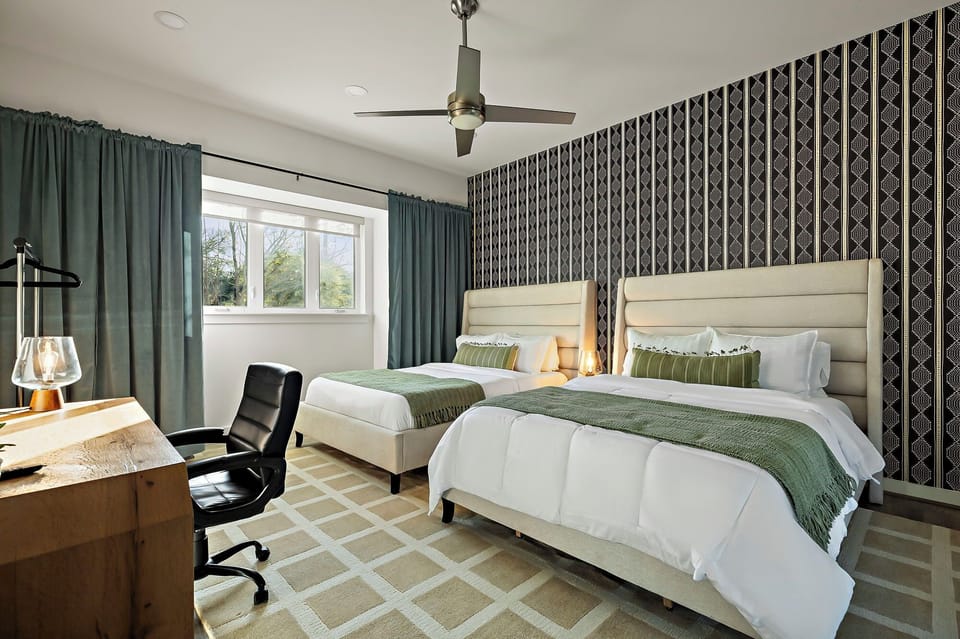 A bedroom featuring two beds, a desk, and patterned wallpaper.
