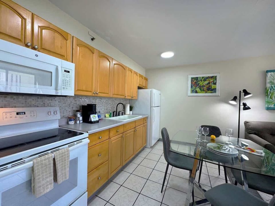 A fully-equipped kitchen featuring light wood cabinets, full-sized appliances, and a modern glass dining table set for a meal!