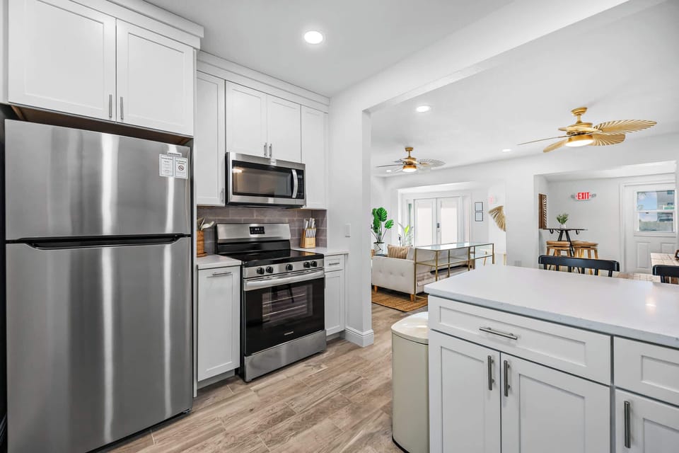 Modern kitchen with stainless steel appliances and white cabinetry opening to a bright living area