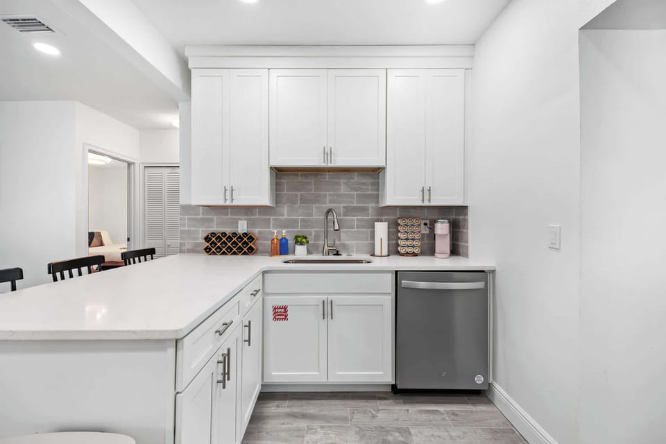 Modern kitchen with white cabinetry, gray tile backsplash, and stainless steel dishwasher.