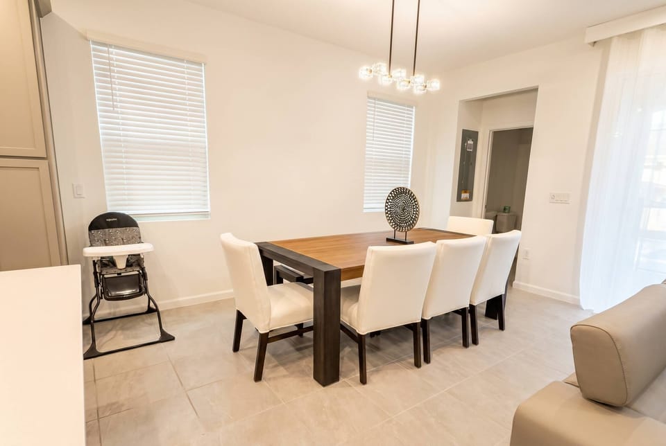 Bright and airy, this dining area features a spacious wooden table surrounded by plush white chairs, perfect for sharing meals. Natural light streams in through the large windows, creating a warm and welcoming atmosphere.