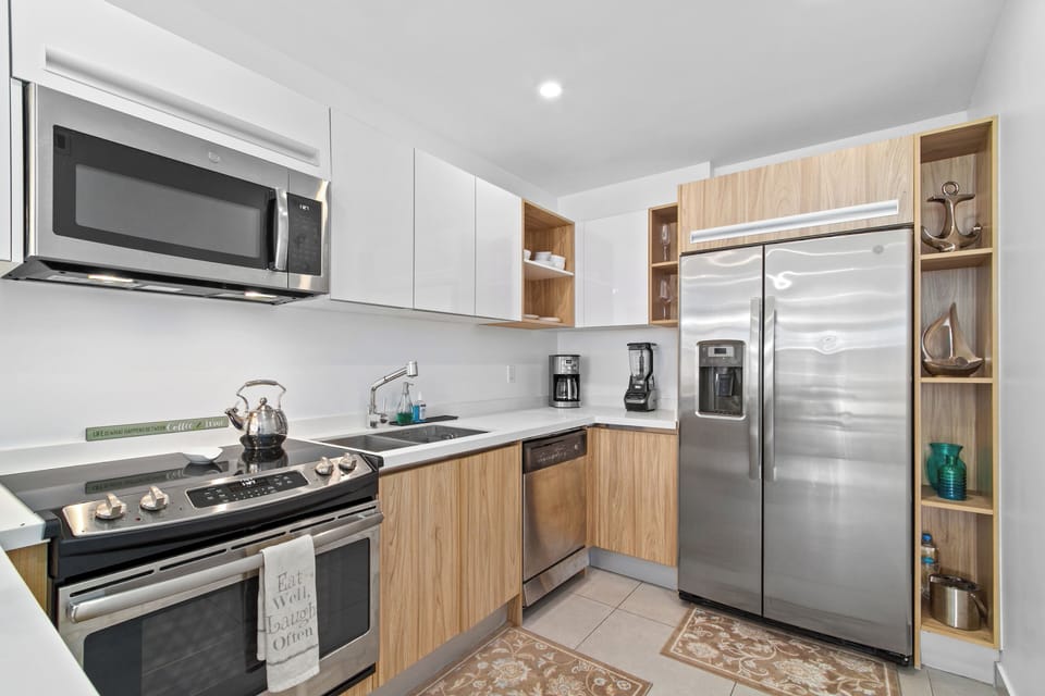A bright, fully equipped kitchen awaits with modern stainless appliances, sleek white and wood cabinetry, and plenty of counter space for preparing your favorite meals.