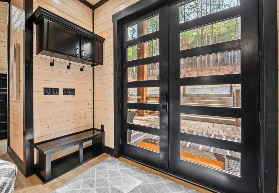 A sleek and modern entryway with floor-to-ceiling glass doors invites you into a home filled with warmth, natural light, and elegant finishes.``